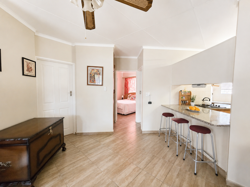 Open plan living area featuring tiled floors, a granite breakfast bar, and a ceiling fan, with a view into the adjacent bedroom.