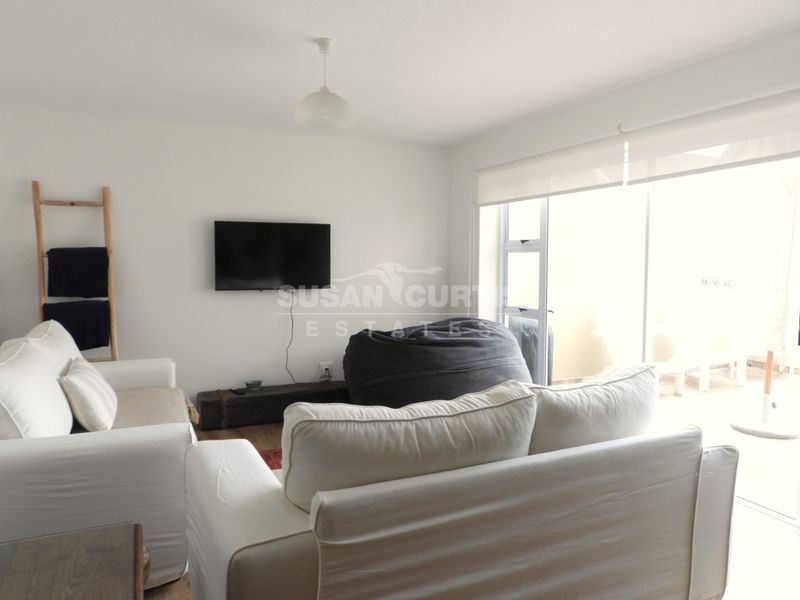A bright living room featuring a sliding glass door with a roller blind, providing natural light and access to the outdoor area.