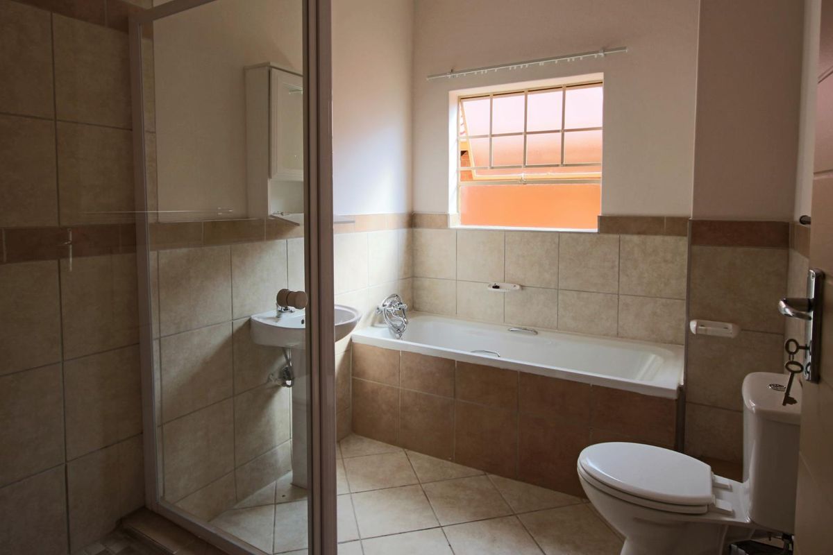 A functional bathroom featuring a shower enclosure, bathtub, pedestal basin, and toilet with neutral wall and floor tiling.