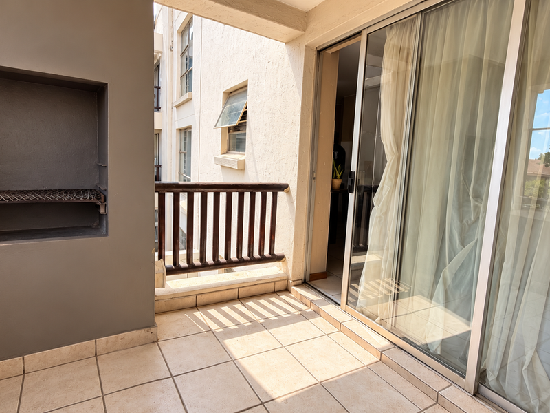 A covered balcony featuring tiled flooring, a built-in braai, and large sliding glass doors providing access to the interior living space.