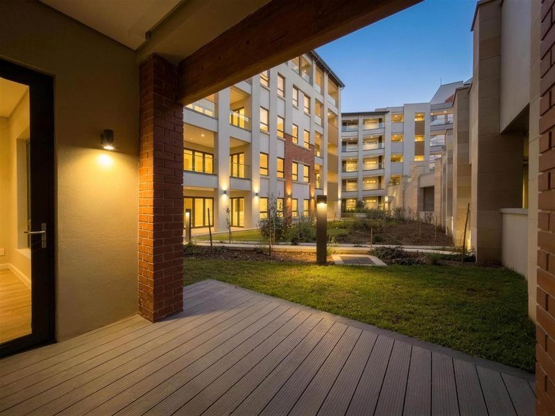 A modern ground-floor patio featuring composite decking, brick accents, and integrated lighting, overlooking a well-maintained communal garden area within the apartment complex.