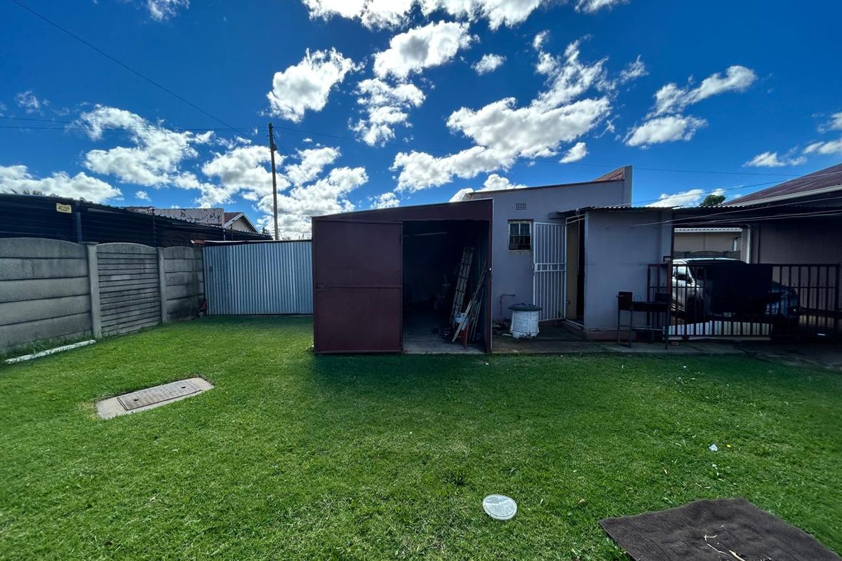 Rear view of the property featuring a lawn, a detached metal garage structure, and perimeter walling.