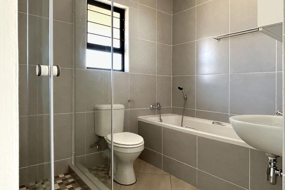A modern bathroom featuring full-height wall tiling, a built-in bathtub with shower mixer, a glass shower enclosure, and a wall-mounted basin.