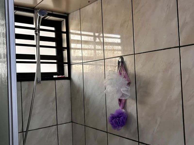 A functional bathroom shower area featuring tiled walls, a shower mixer, and a window with security bars.
