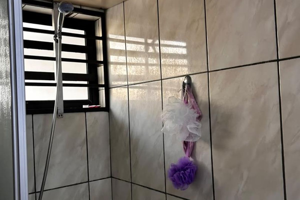 A functional bathroom shower area featuring tiled walls, a shower mixer, and a window with security bars.