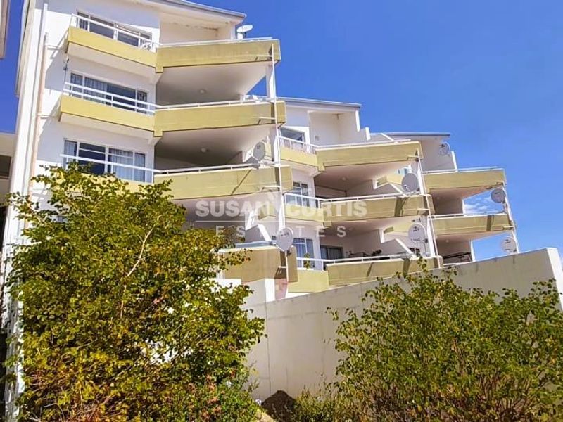 Exterior view of a multi-story apartment building featuring tiered balconies, concrete stair access, and a retaining wall.