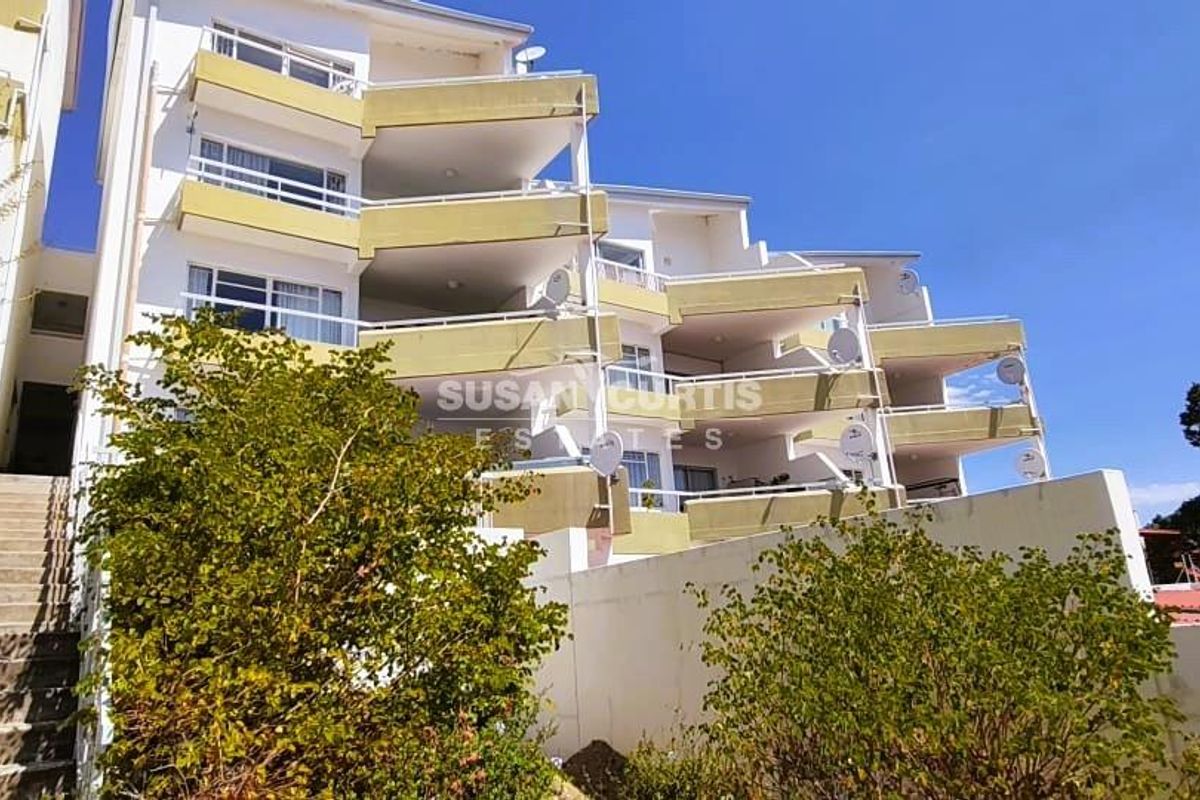Exterior view of a multi-story apartment building featuring tiered balconies, concrete stair access, and a retaining wall.