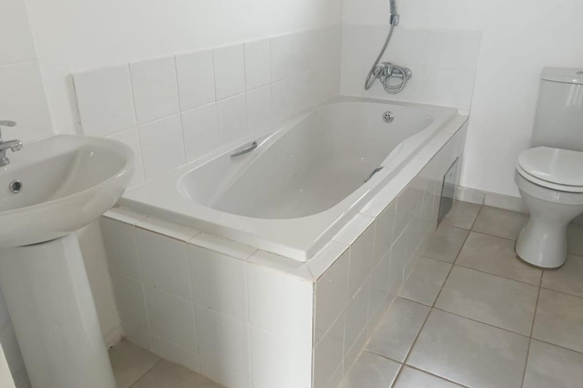 A functional bathroom featuring a white pedestal basin, a tiled bathtub with a handheld shower attachment, and a standard toilet.