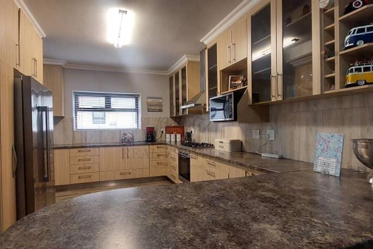 A functional kitchen featuring light wood-tone cabinetry, dark laminate countertops, built-in appliances, and ample storage space with glass-fronted display units.