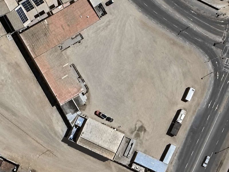 Aerial view of a commercial property featuring multiple buildings with metal roofing, solar panels, and a large unpaved yard area adjacent to a main road.