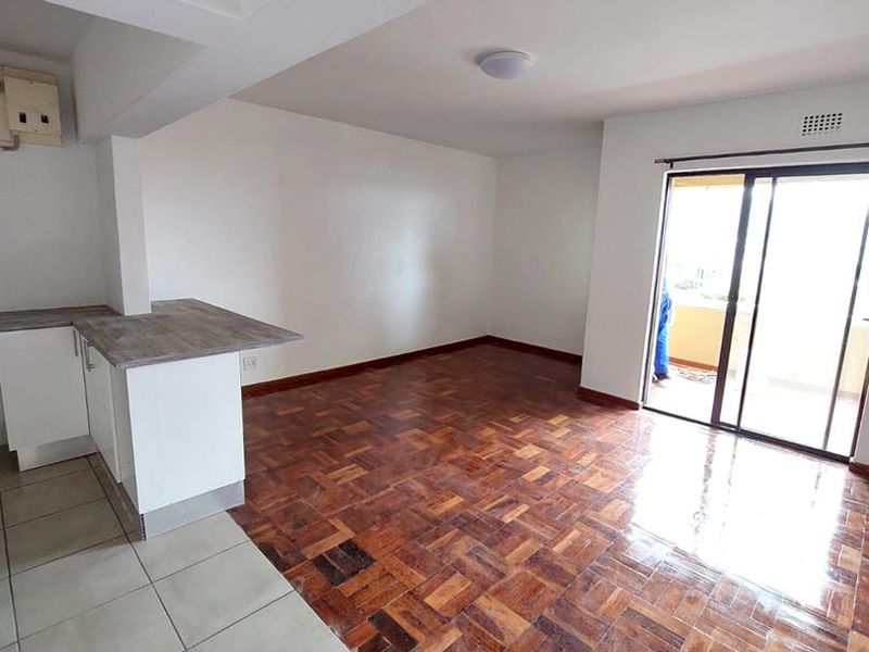 An open-plan living and kitchen area featuring polished parquet flooring, tiled kitchen zone, and sliding glass doors leading to a balcony.