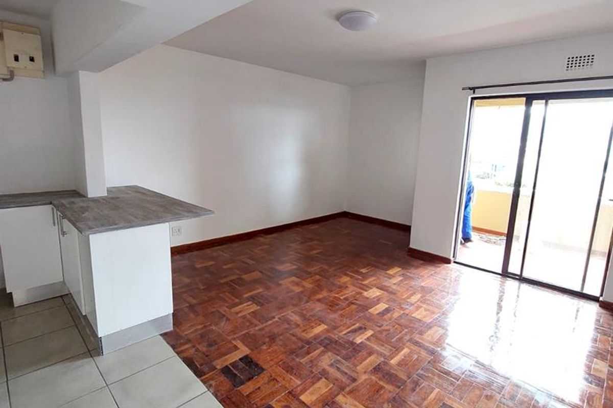 An open-plan living and kitchen area featuring polished parquet flooring, tiled kitchen zone, and sliding glass doors leading to a balcony.