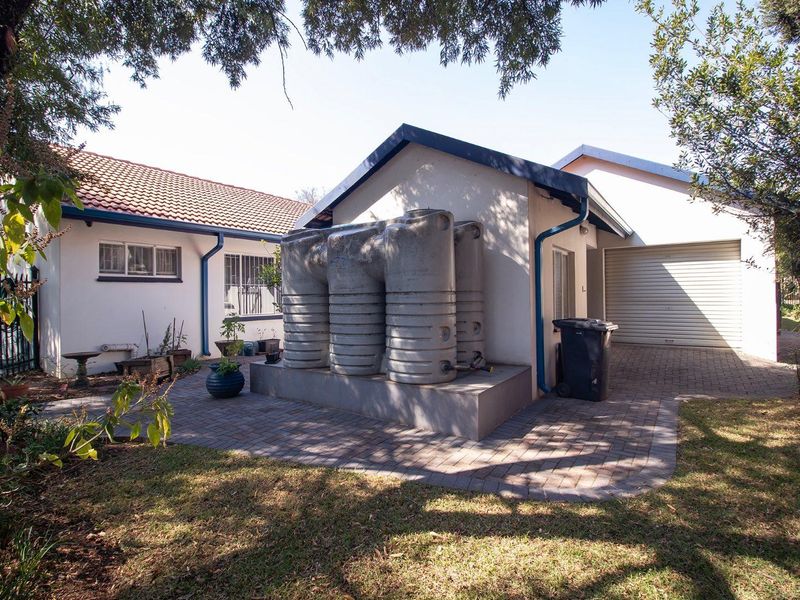 Rear exterior view showing a paved patio area, garage access, and a set of installed water storage tanks.