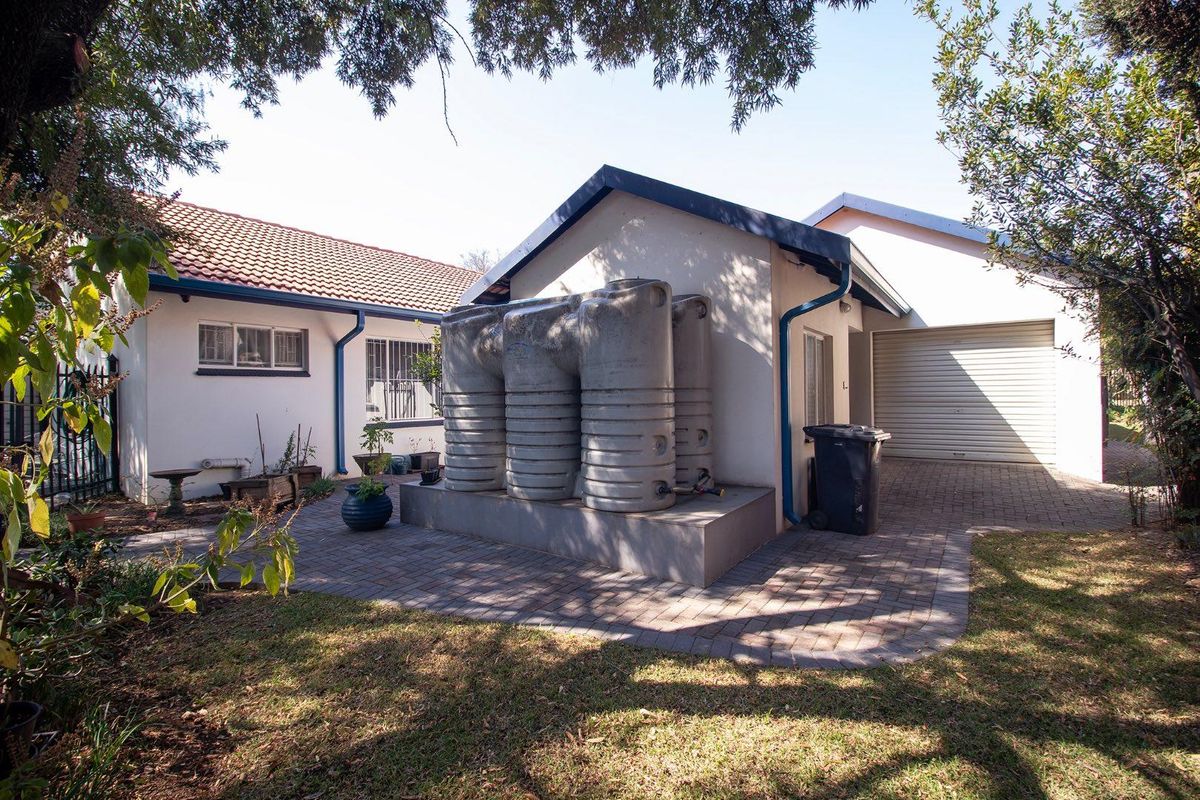 Rear exterior view showing a paved patio area, garage access, and a set of installed water storage tanks.