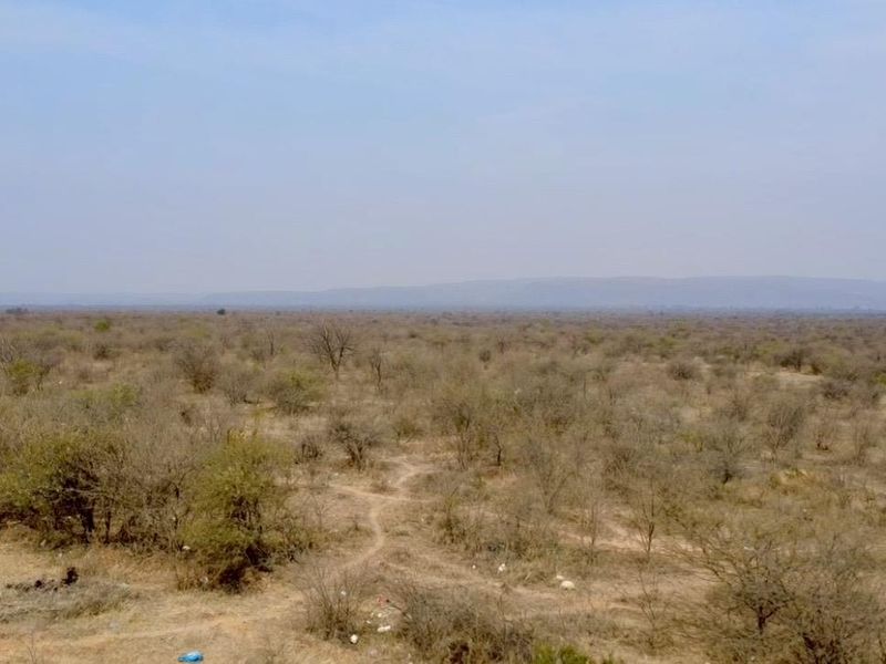 An expansive aerial view of the natural farm landscape featuring dry bushveld vegetation and distant mountain ranges.