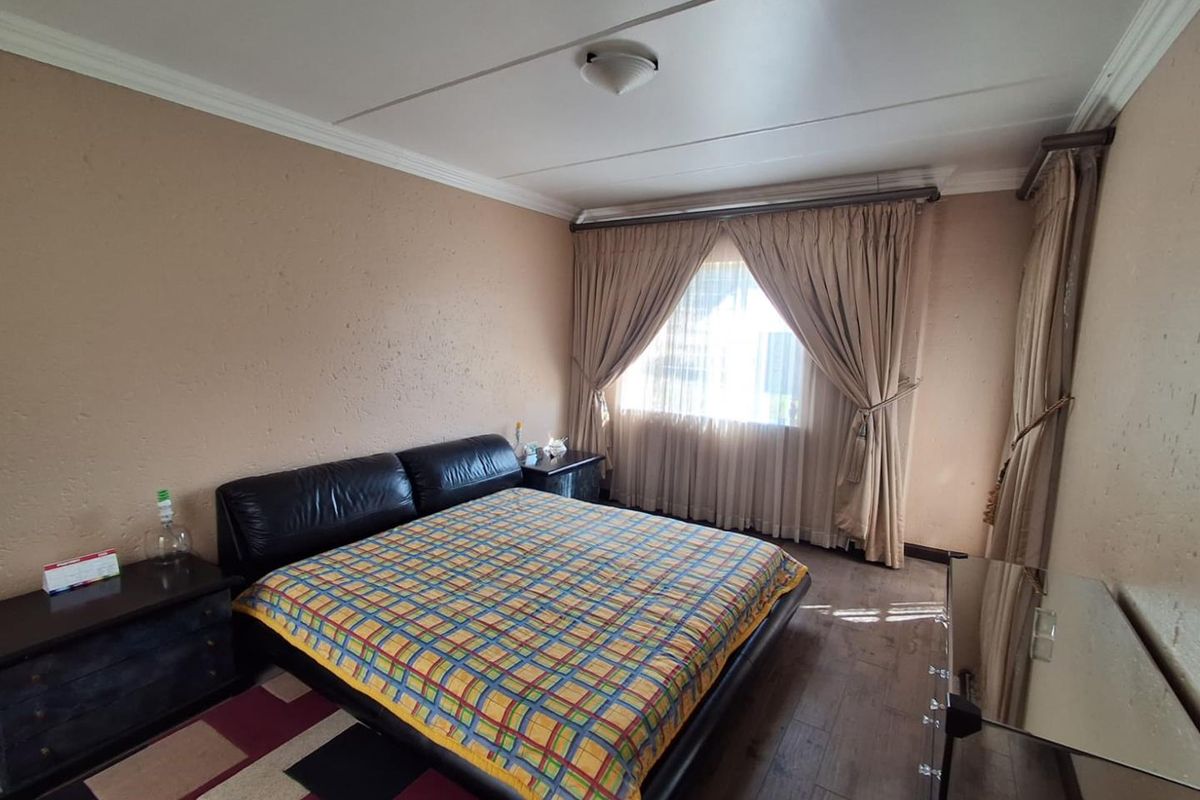 A spacious bedroom featuring wood-look flooring, textured walls, and large windows with fitted curtain tracks.