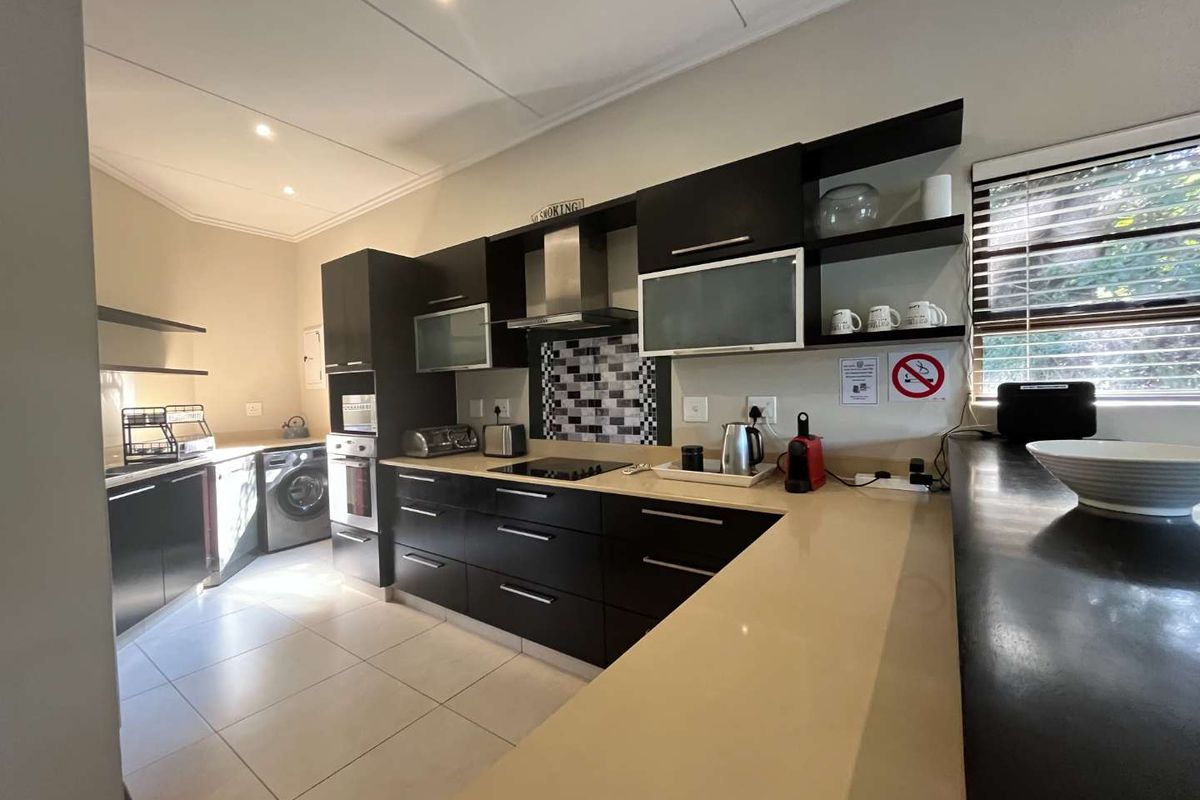 Modern kitchen featuring dark cabinetry, stone countertops, built-in oven, extractor fan, and integrated laundry space with tiled flooring.