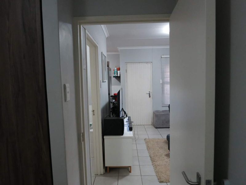 A view from a doorway looking into a tiled hallway leading towards a living area with neutral wall finishes.