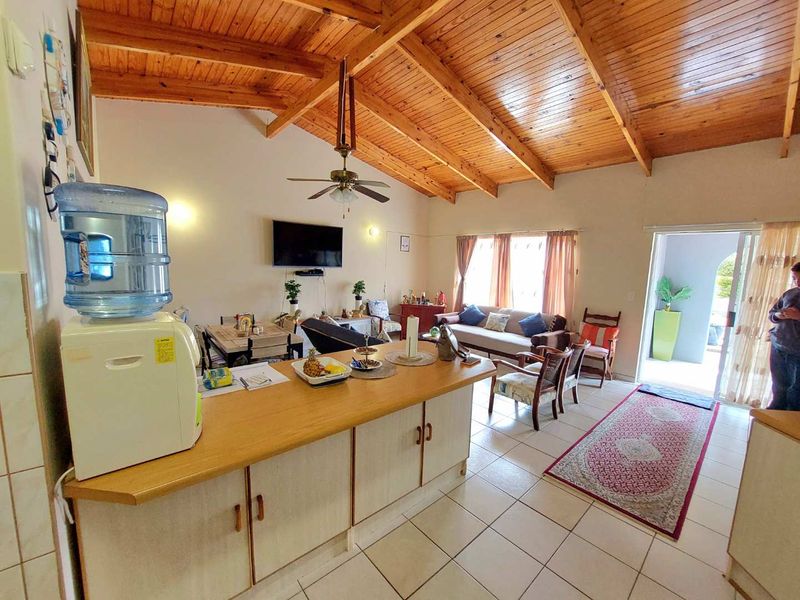 Spacious open-plan living area featuring a high exposed timber beam ceiling, tiled flooring, and a central kitchen island with direct access to the patio.