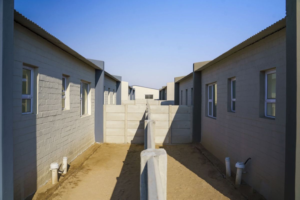 Rear exterior view of townhouse units featuring precast concrete boundary walls and unlandscaped sandy yard space.
