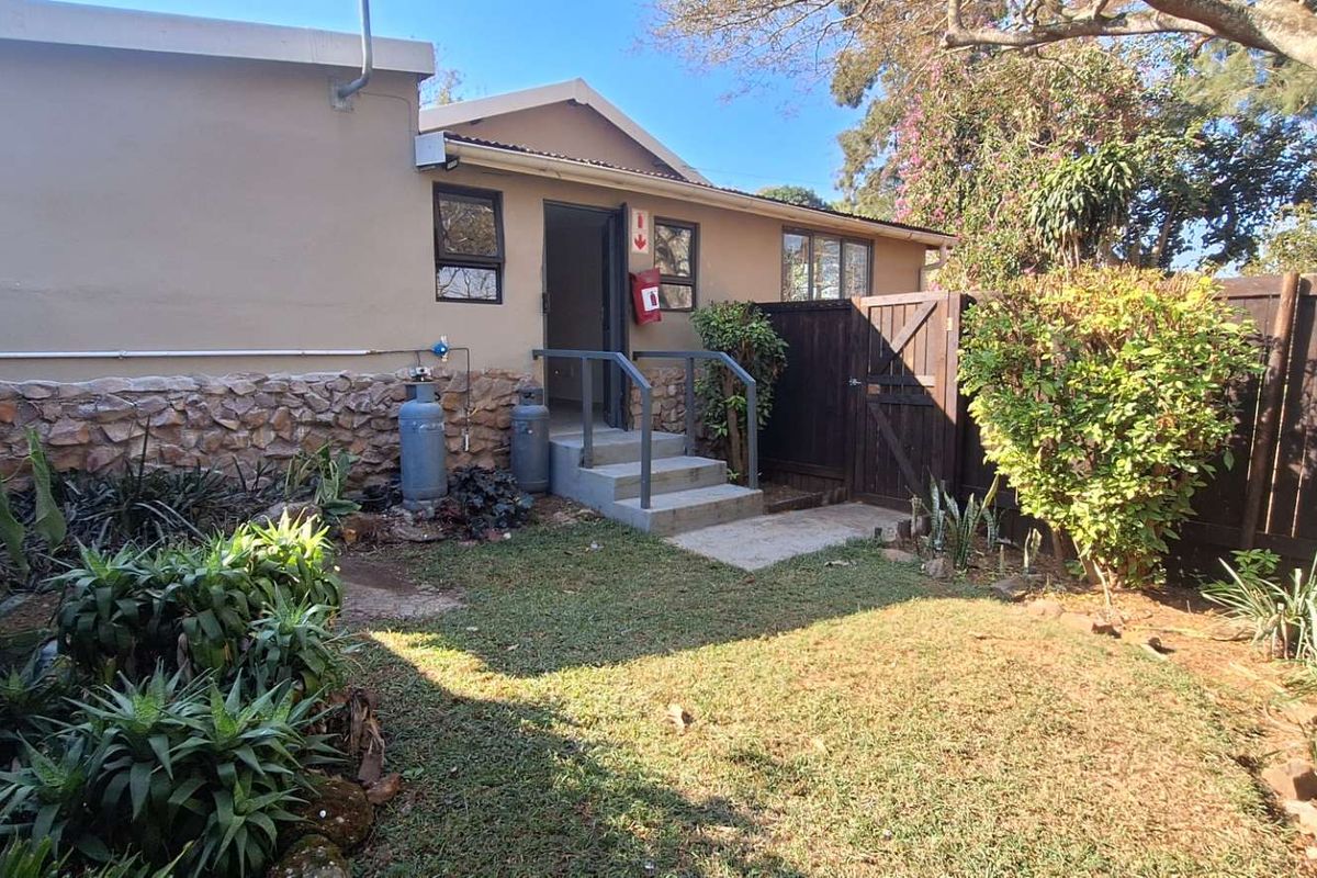 Rear exterior view of the apartment featuring a small garden, stone-clad wall detail, concrete steps, and secure timber fencing.