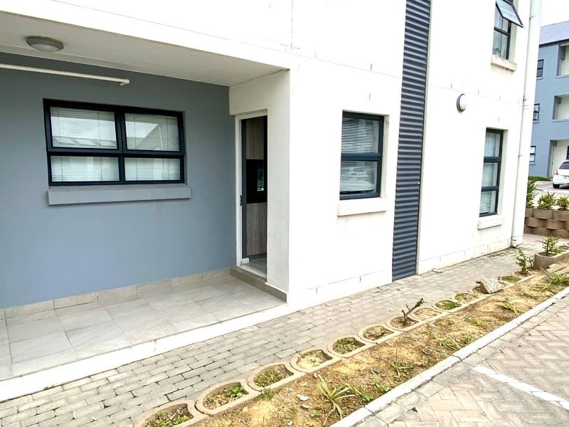 Front exterior view of the apartment featuring a covered tiled patio, paved walkway, and modern aluminium window frames.