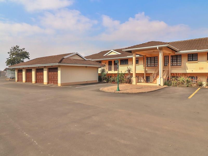 Exterior view of an apartment complex featuring a paved driveway, multiple garage units, and a covered entrance with balcony access.
