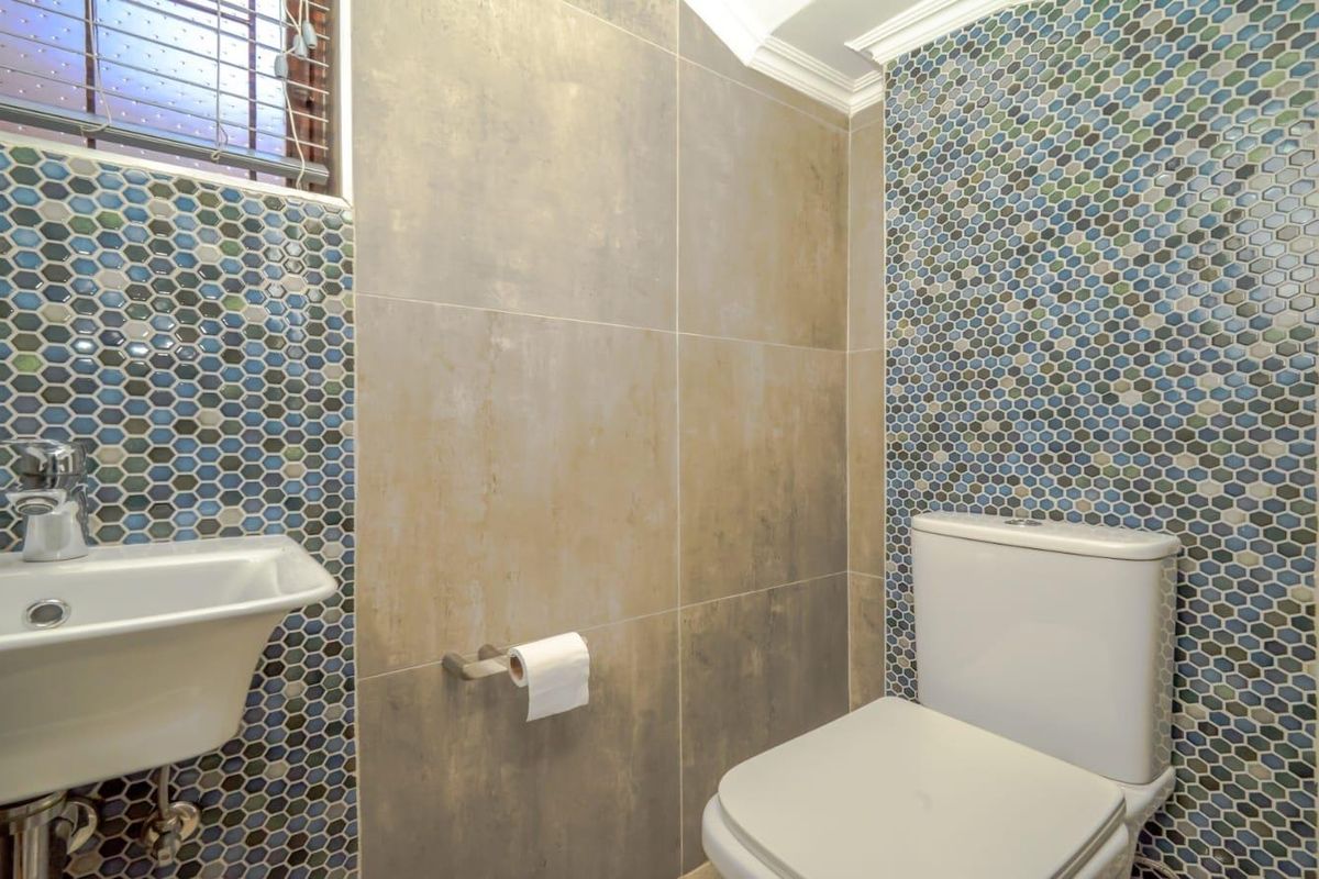 A modern bathroom featuring a wall-mounted basin, a dual-flush toilet, and decorative hexagonal mosaic tile accents paired with large-format neutral wall tiles.