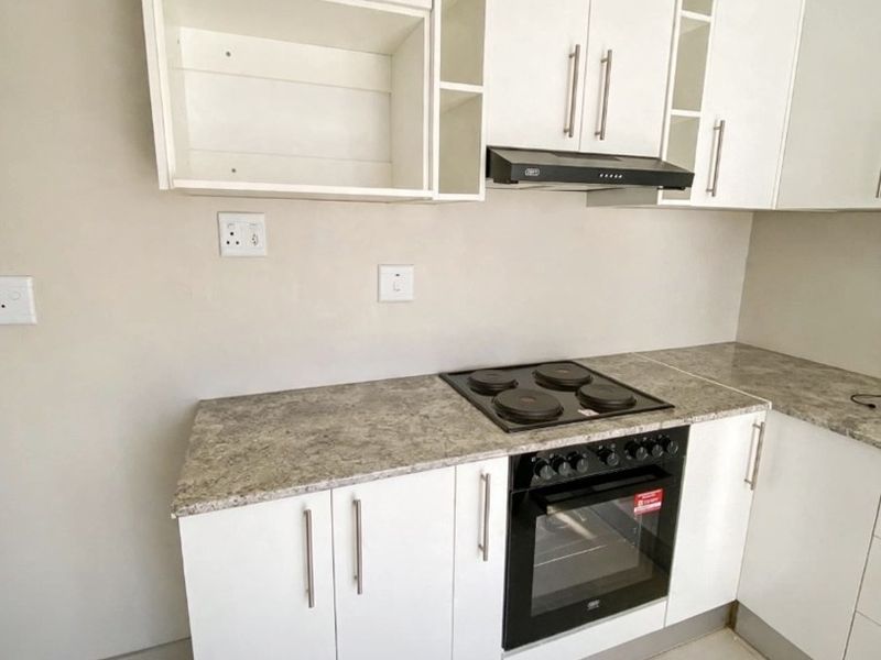 A clean, modern kitchen featuring white cabinetry, stone-look laminate countertops, and integrated electric cooking appliances.