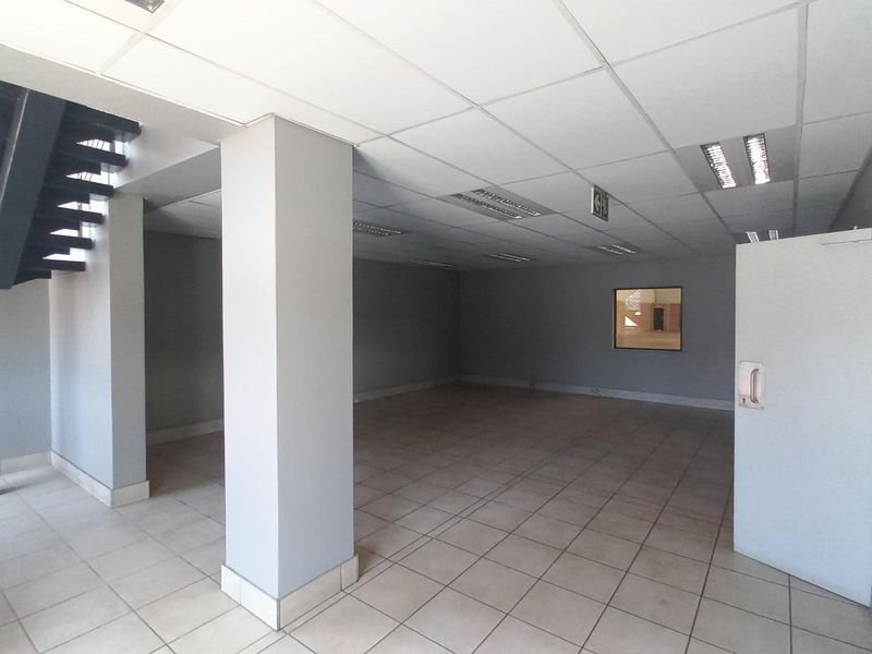 An open-plan industrial office space featuring ceramic tiled flooring, a suspended ceiling with recessed lighting, and an internal metal staircase.