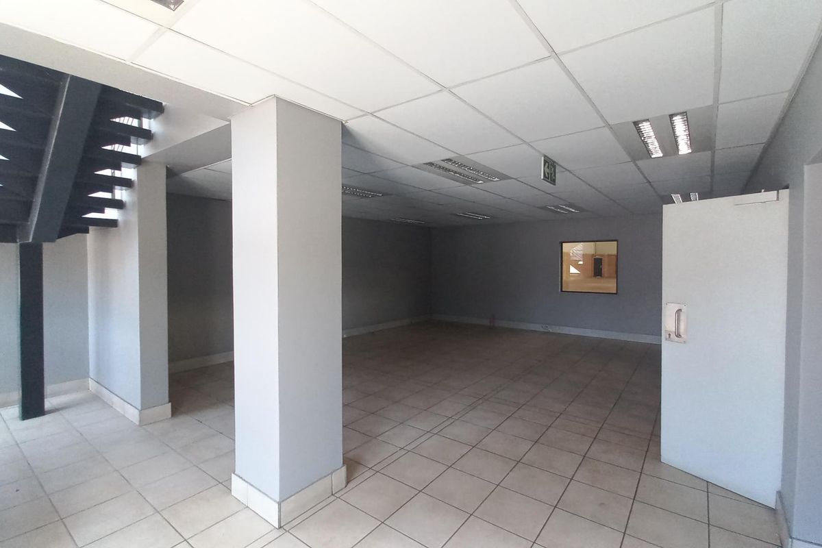 An open-plan industrial office space featuring ceramic tiled flooring, a suspended ceiling with recessed lighting, and an internal metal staircase.
