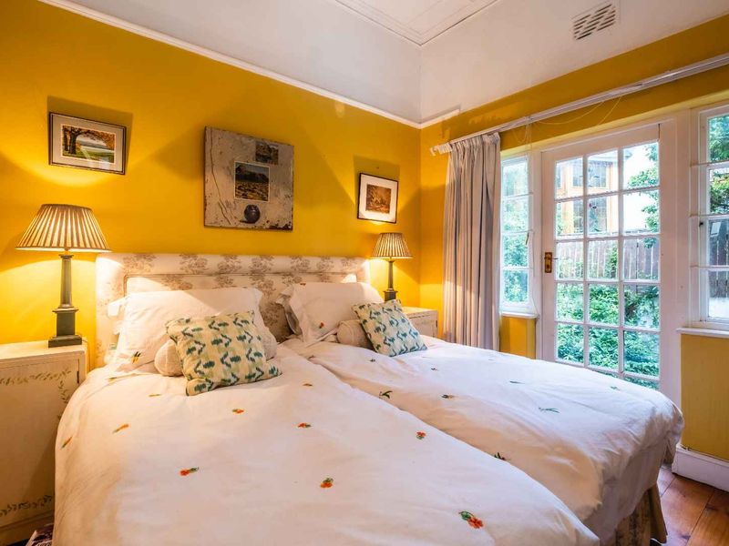 A cozy bedroom featuring warm yellow walls, timber flooring, and direct access to the garden through classic French doors.