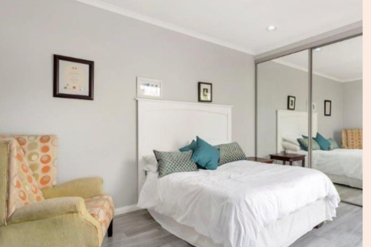 A well-maintained bedroom featuring light-toned wood-look flooring, recessed ceiling lighting, and large floor-to-ceiling mirrored sliding wardrobe doors.