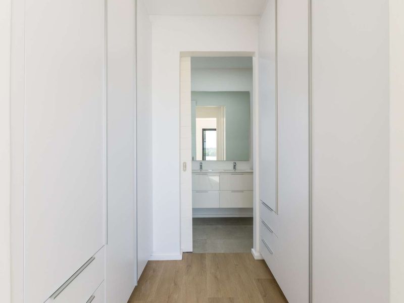 A clean, modern hallway featuring extensive built-in cabinetry and light wood-look flooring, leading directly into a bright, contemporary bathroom.