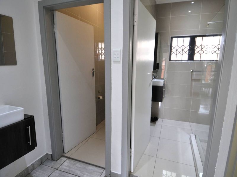 A clean, modern bathroom featuring a wall-mounted vanity, tiled flooring, and a separate shower area with a security-fitted window.