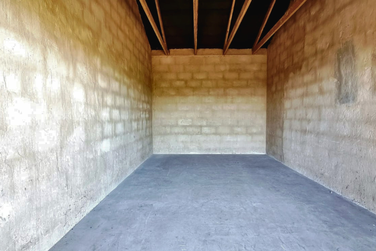 An unfinished utility space featuring exposed concrete block walls and open roof rafters, suitable for storage or further development.