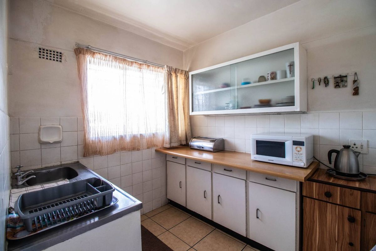 A compact kitchen featuring white cabinetry, a wooden countertop, tiled splashbacks, and a stainless steel sink, offering a functional layout with potential for modernization.