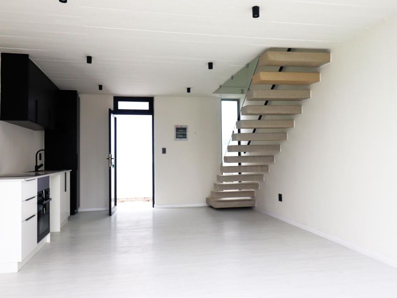 Modern open-plan living area featuring a sleek kitchen with built-in appliances and a striking floating staircase with glass balustrade.