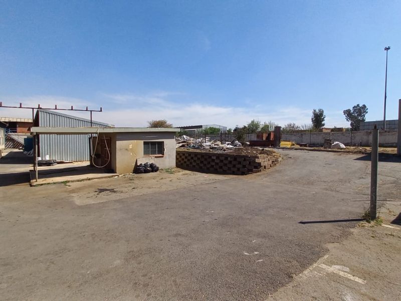 Expansive industrial yard area featuring asphalt surfacing, perimeter walling, and metal-clad structures, suitable for storage or logistics operations.