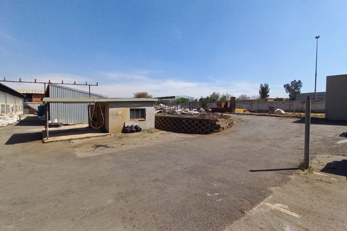 Expansive industrial yard area featuring asphalt surfacing, perimeter walling, and metal-clad structures, suitable for storage or logistics operations.