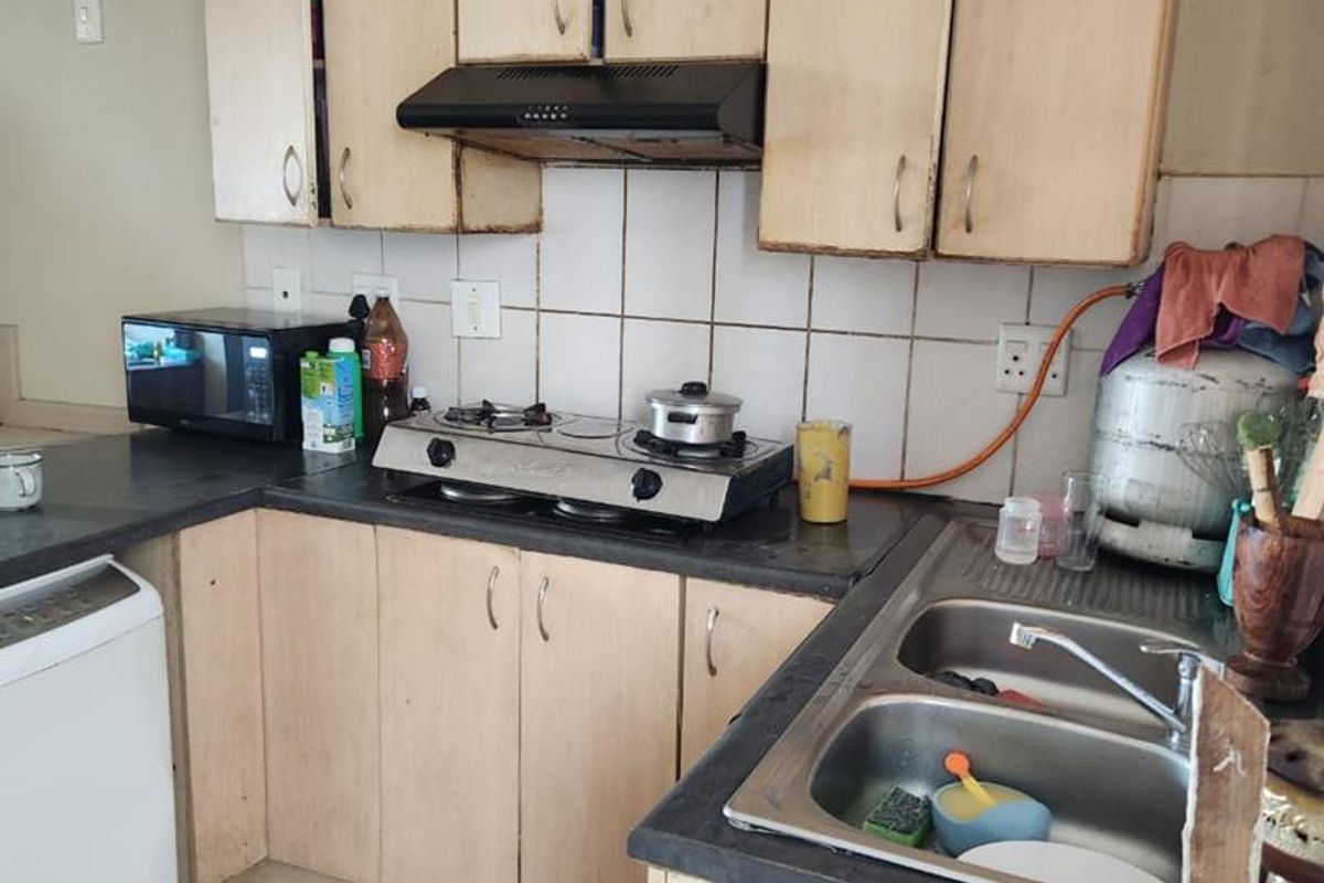 A functional kitchen featuring laminate cabinetry, a gas hob with extractor fan, and a double bowl stainless steel sink with tiled backsplash.