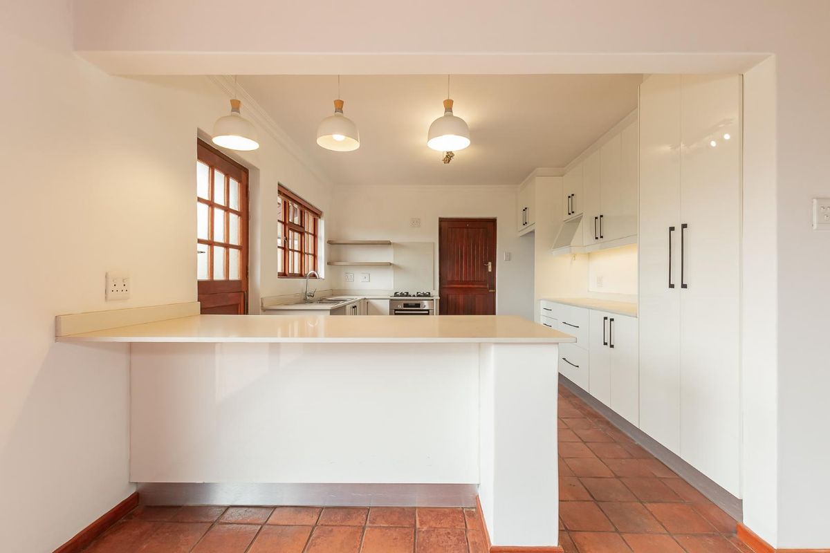 A clean, well-lit kitchen featuring white built-in cabinetry, a breakfast counter, and terracotta floor tiles, offering a functional and bright workspace.
