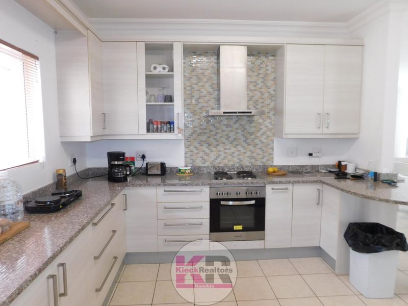 Modern kitchen featuring light wood-grain cabinetry, granite countertops, a built-in oven with gas hob, and a decorative mosaic tile backsplash.