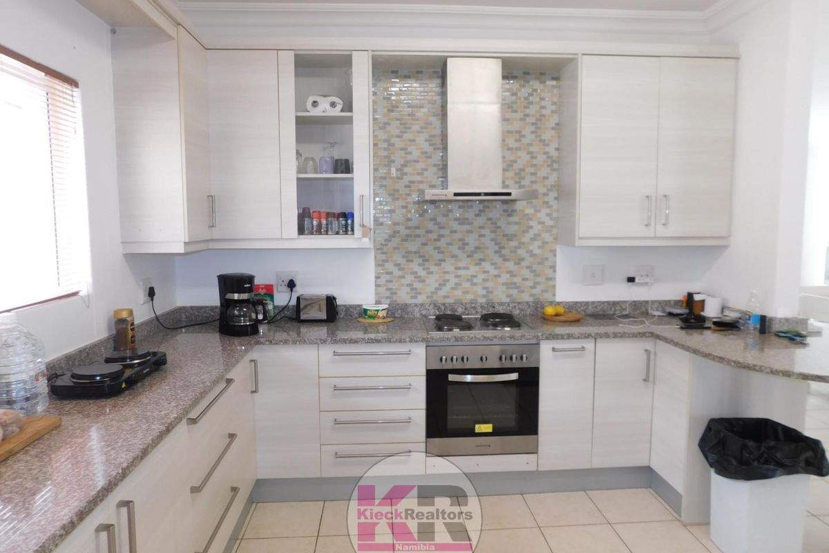 Modern kitchen featuring light wood-grain cabinetry, granite countertops, a built-in oven with gas hob, and a decorative mosaic tile backsplash.