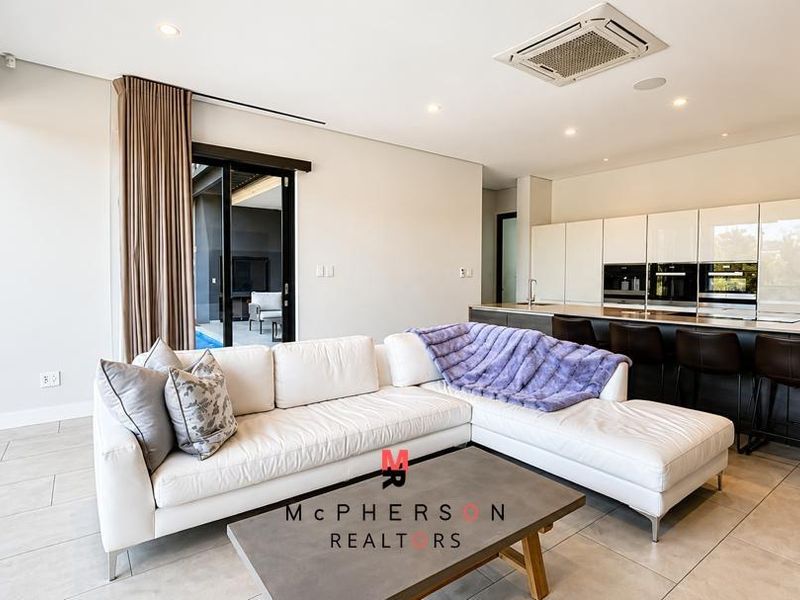 Modern open-plan living area featuring a sleek kitchen with integrated appliances, recessed lighting, and large sliding doors opening to an outdoor patio.