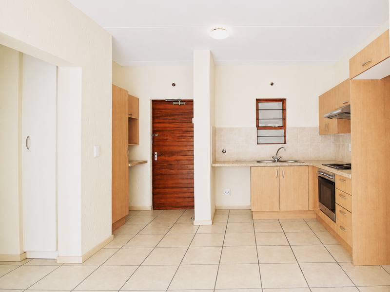 A functional, empty kitchen featuring light wood cabinetry, tiled flooring, a built-in oven, and a tiled backsplash, offering a clean canvas for updates.