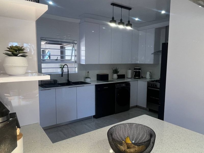 Modern kitchen featuring high-gloss white cabinetry, quartz countertops, integrated appliances, and a stylish stone feature wall with contemporary lighting.