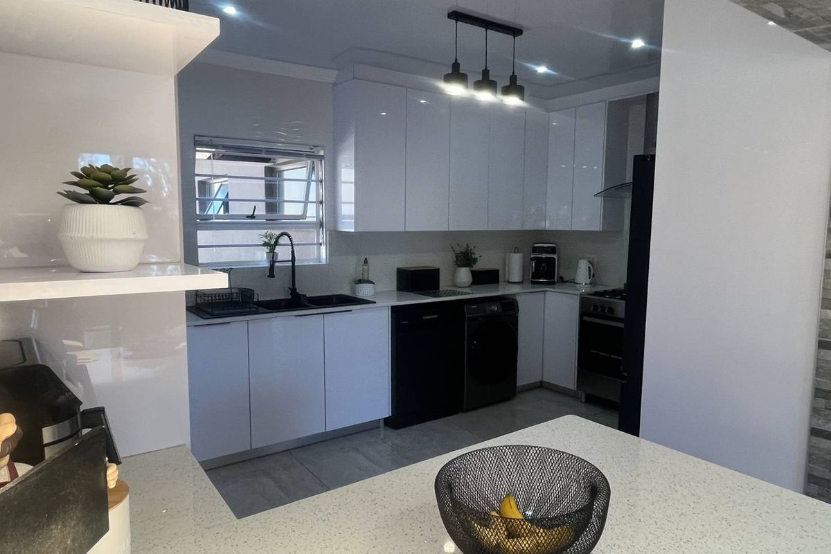 Modern kitchen featuring high-gloss white cabinetry, quartz countertops, integrated appliances, and a stylish stone feature wall with contemporary lighting.