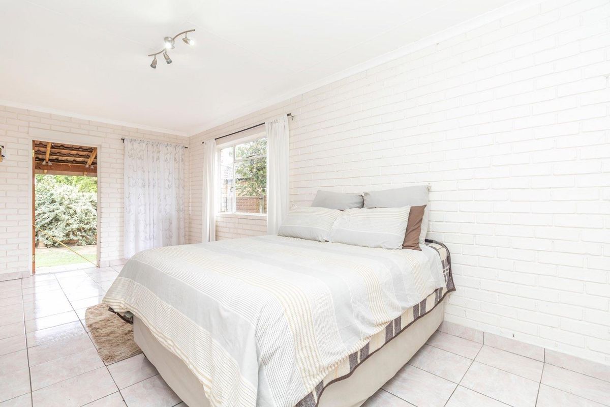 A bright bedroom featuring painted brick walls, tiled flooring, and direct access to an outdoor patio area.