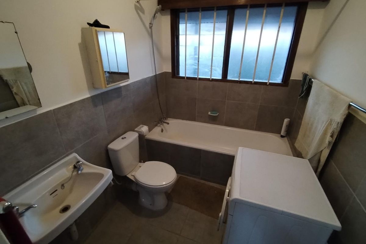 A functional bathroom featuring a bathtub, toilet, and washbasin with neutral wall tiling and window security bars.